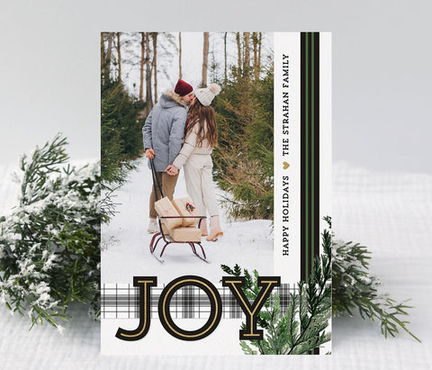 holiday card in portrait orientation with a single photo, black and green ribbon, plaid ribbon, large JOY text and evergreen branch detail